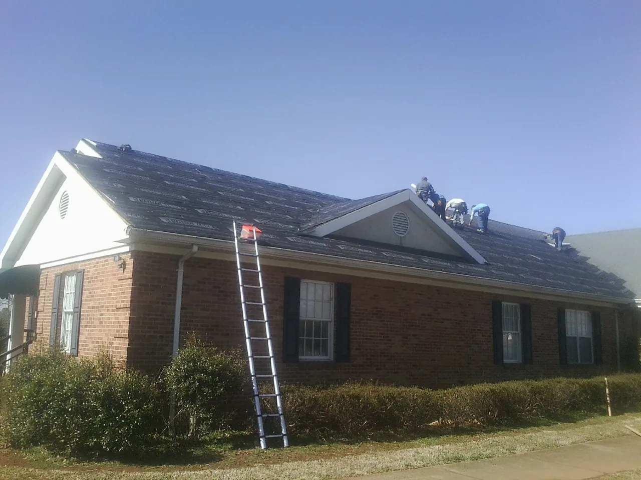 Crew tearing shingles off a brick ranch roof with a ladder set — Emergency Roof Repair work by our crew in Allamuchy