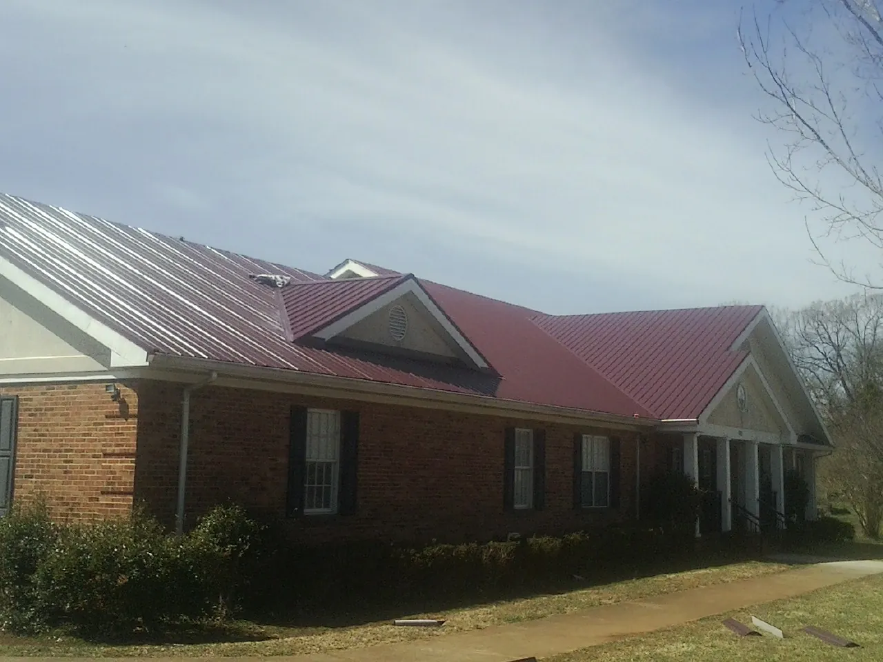 Red metal roof with gabled entries on a long brick building, from a Hail Damage Roof Repair job in Allamuchy
