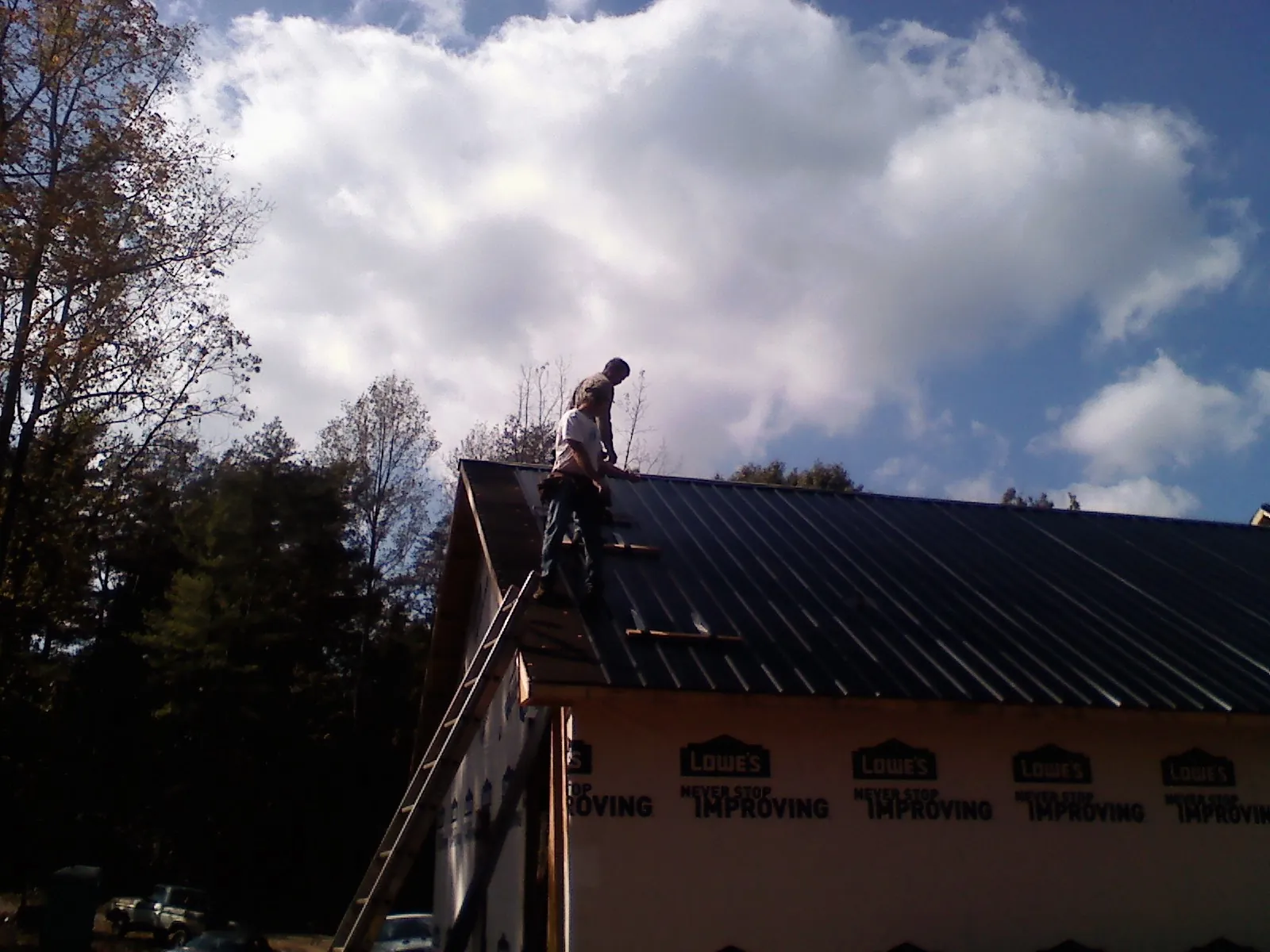 Roofer fastening dark metal panels high against a cloudy sky, from a Roof Inspection job in Allamuchy