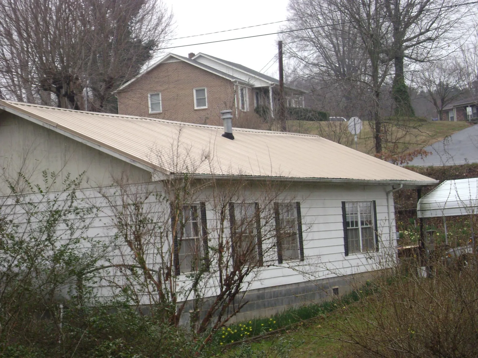 Tan metal roof on a white sided house set into a hillside — Commercial Roofing by Roofing Brothers in Allamuchy